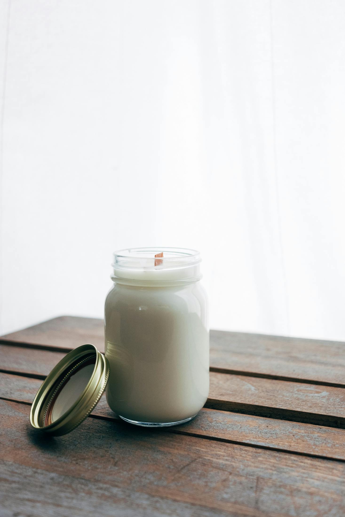 A simple jar candle with wooden wick on rustic table.