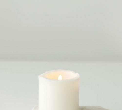 Elegant lit white candle on a marble slab creating a minimalist and tranquil setting.